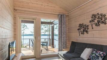 Un interior de madera con un sofá, un televisor y vista a un lago a través de una puerta de cristal.