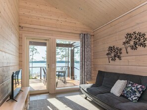 Un intérieur en bois avec un canapé, un téléviseur et une vue sur un lac, visible à travers une porte vitrée.