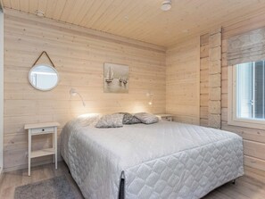 Een slaapkamer met een bed, nachtkastje, spiegel en een raam met zonwering.
