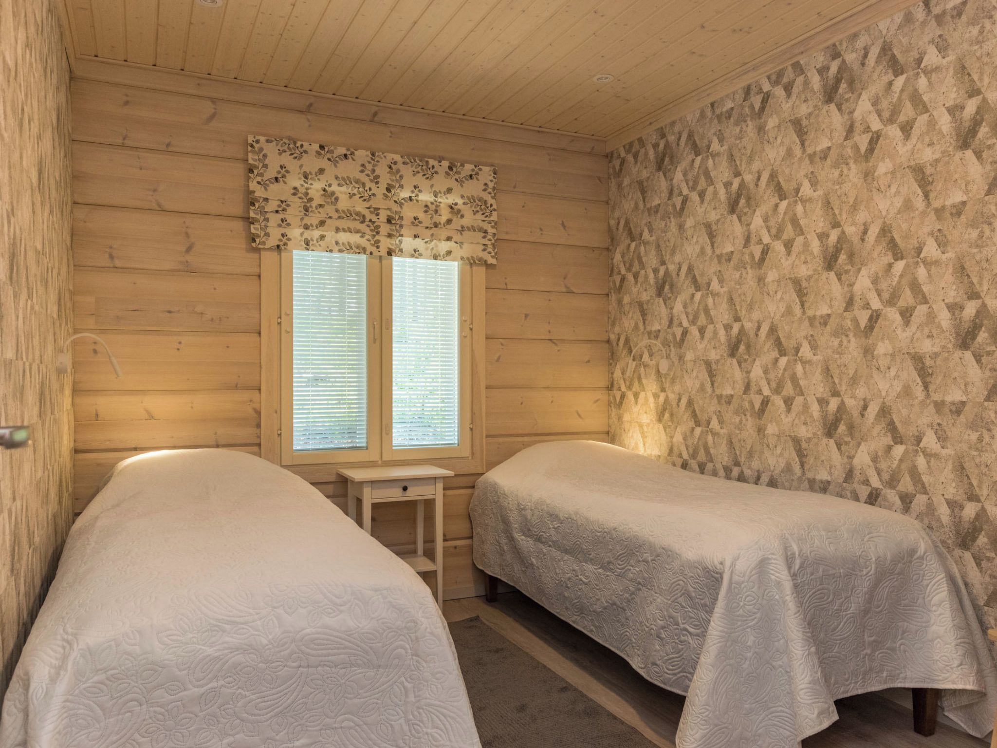 Een kamer met twee eenpersoonsbedden, een tafeltje en een raam met jaloezieën.