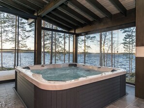 Een jacuzzi in een overdekte ruimte met uitzicht op een meer en bomen.