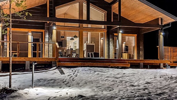 Una cabaña de troncos moderna con una amplia terraza, ventanas grandes y un techo a dos aguas destacado.