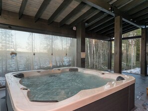 A hot tub under a covered area with a view of a forest and a body of water.