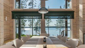 Un comedor moderno con una gran mesa, sillas y vistas a un lago y un bosque.