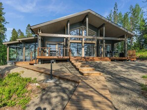 Une cabane en rondins moderne dotée d’une grande façade vitrée, d’une terrasse en bois et d’un espace salon extérieur.