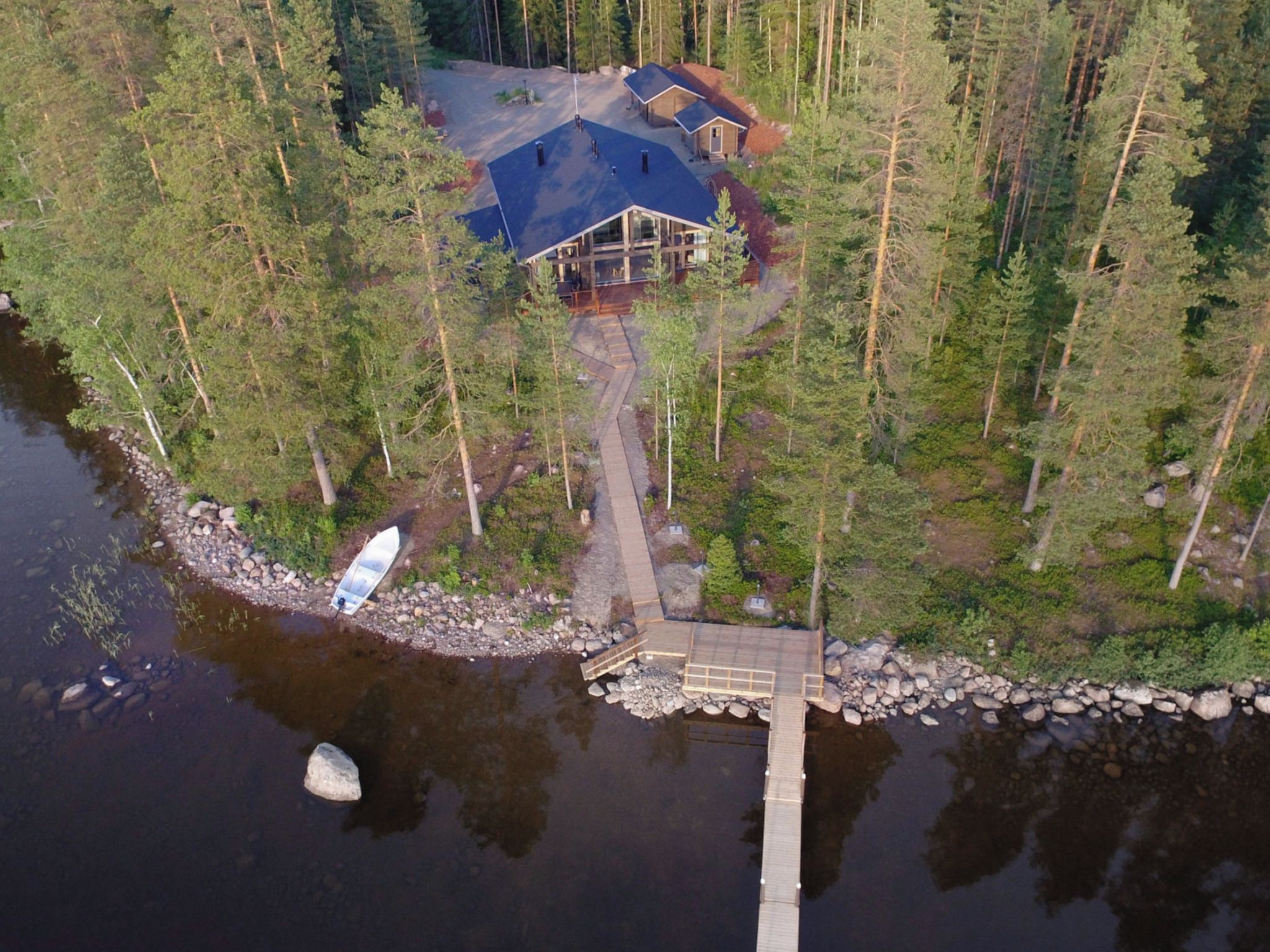 Eine Holzhütte mit einem Steg, der in einen See führt, umgeben von dichtem Wald.