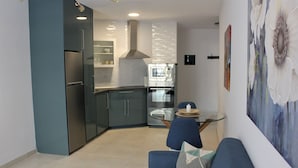 Una cocina moderna con refrigerador, horno y microondas. Hay una zona de comedor con una mesa y sillas. Un sofá con cojín está en primer plano.