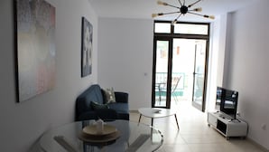 Una sala moderna con una mesa de vidrio, un sofá azul y un televisor sobre un mueble.