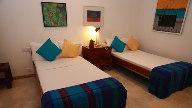 Habitación de hotel con dos camas, cada una con una colcha a rayas, una mesita de noche con lámpara y un teléfono en la pared.