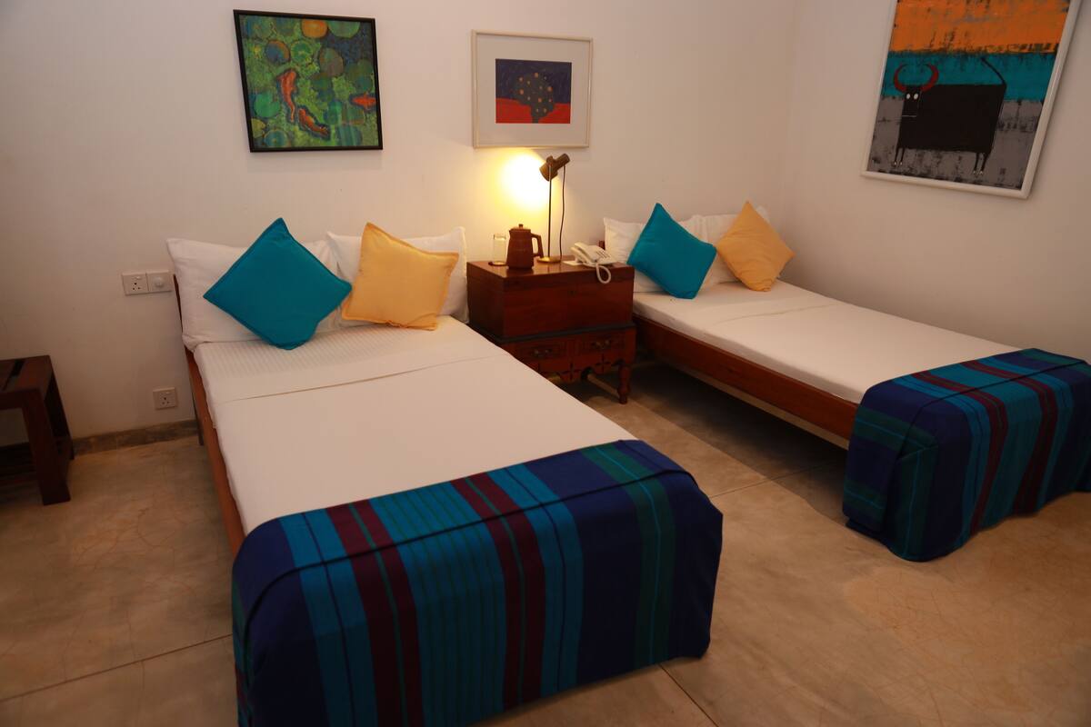A hotel room with two beds, each with a striped bedspread, a bedside table with a lamp, and a wall-mounted phone.