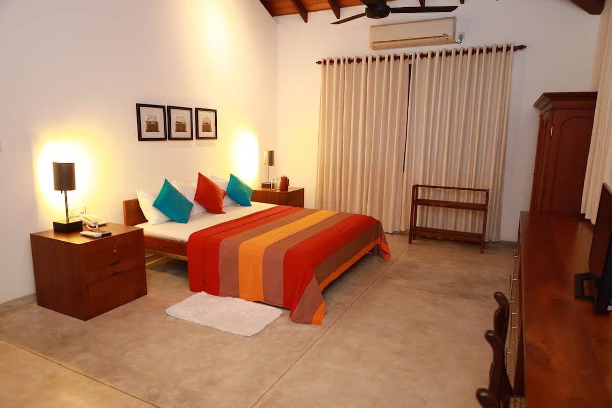 A bedroom with a bed, bedside tables, a lamp, a chair, a small table, and a window with curtains.