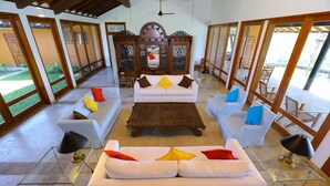 A spacious living area with a central white sofa, two side sofas, and a wooden coffee table. The room features large windows and a view of the outdoors. - Makuludola Bungalow (Malimbada)