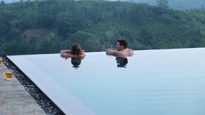 Dos personas descansando en una piscina infinita transparente con vistas a una ladera boscosa.