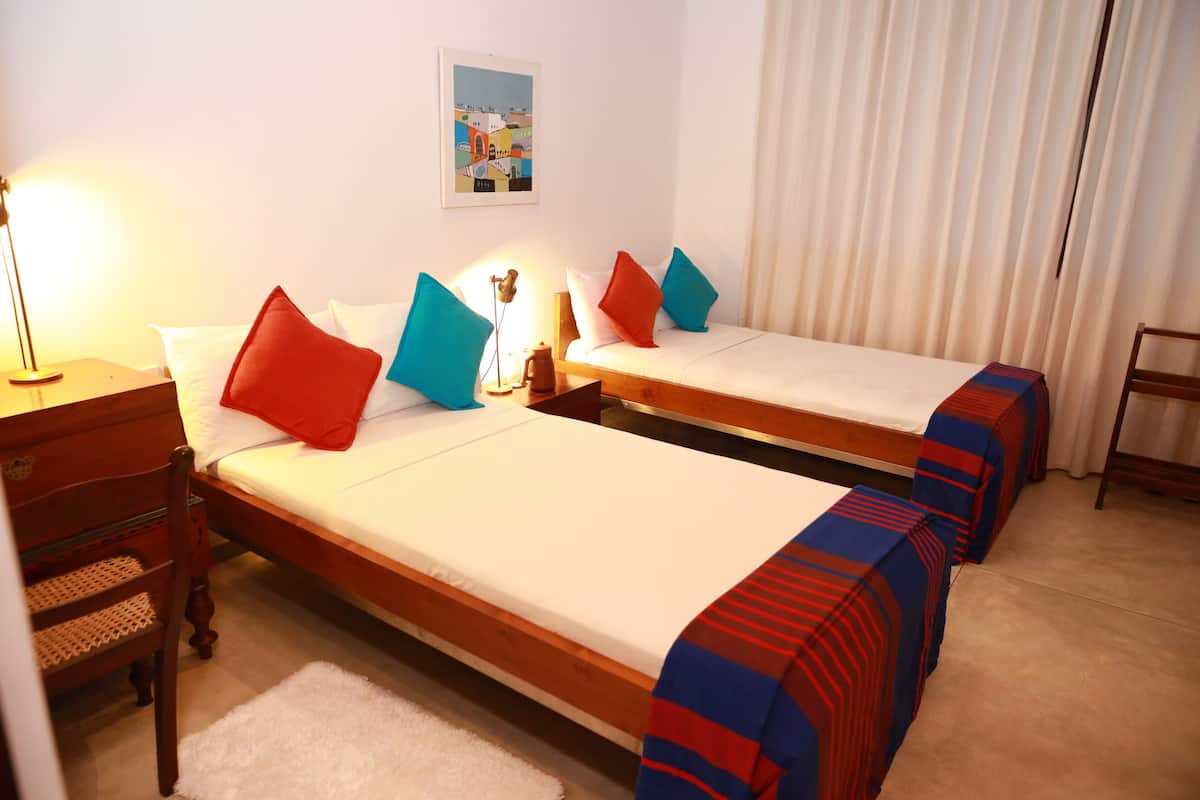 A hotel room with two single beds, each with a red and blue striped blanket, a wooden nightstand with a lamp, and a small table with a decorative item.