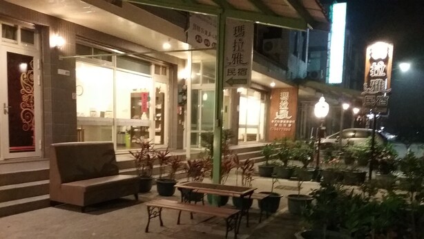 A night view of a restaurant with outdoor seating, including a sofa and tables. There are potted plants around the seating area. - Malaya Guesthouse (Budai)