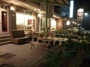 A night view of a restaurant with outdoor seating, including a sofa and tables. There are potted plants around the seating area. - Malaya Guesthouse (Budai)