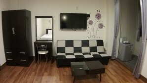 A living room with a black and white checkered sofa, a TV mounted on the wall, a wardrobe, a small table, and a mirror. - Malaya Guesthouse (Budai)
