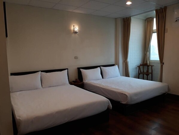 A hotel room with two single beds, a small table, and a chair.