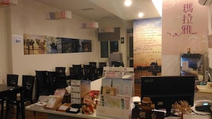 A reception area with a desk, chairs, and informational posters. - Malaya Guesthouse (Budai)
