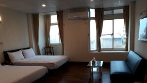 A hotel room with two single beds, a sofa, a small table, and a window with curtains. - Malaya Guesthouse (Budai)