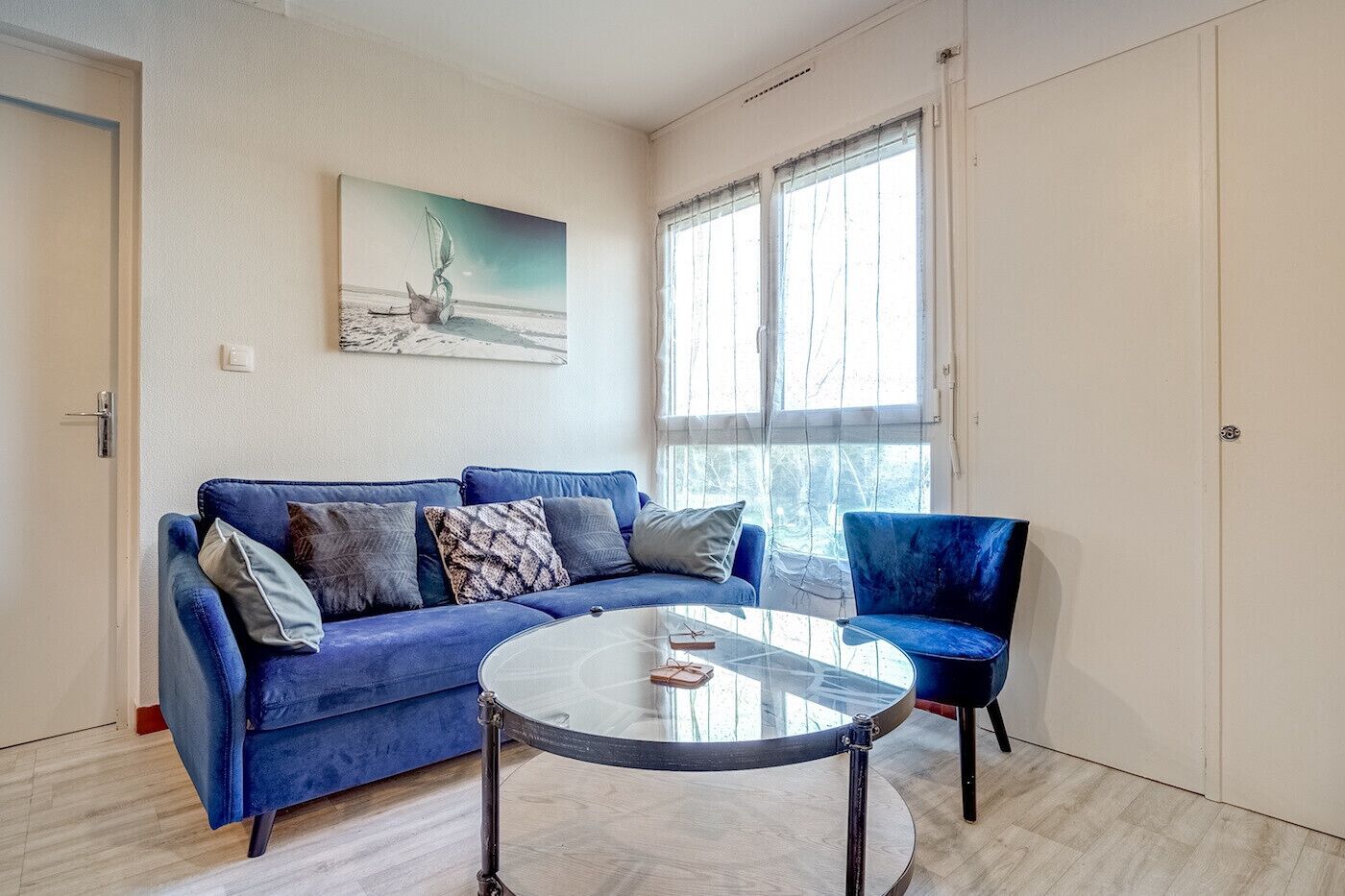Una sala de estar moderna con un sofá azul, una mesa de centro de vidrio y una silla.