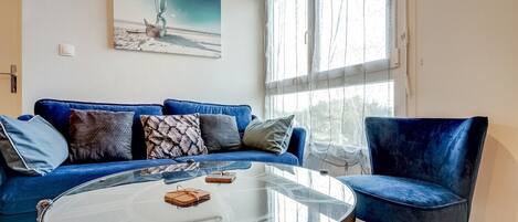 A living room with a blue sofa, a glass coffee table, and a painting of a sailboat on the wall.