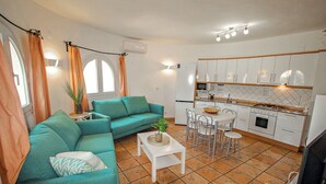 A compact living space with a teal sofa, a small dining table, and a kitchen area with white cabinets and a tiled floor. - May - pretty holiday property with private pool in Benissa (Benissa)