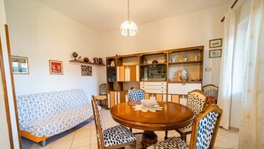 A dining area with a round wooden table, six chairs, a sofa, and a chandelier. - Apartment Lo Scoglio in Portoferraio (Portoferraio)
