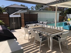 A patio area with a table and chairs, a pool, and a covered seating area. - Spacious Resort Style Family Beach House (Beacon Hill)