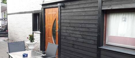 Un pequeño espacio al aire libre con una mesa y sillas, una puerta de madera y una ventana con cortina.