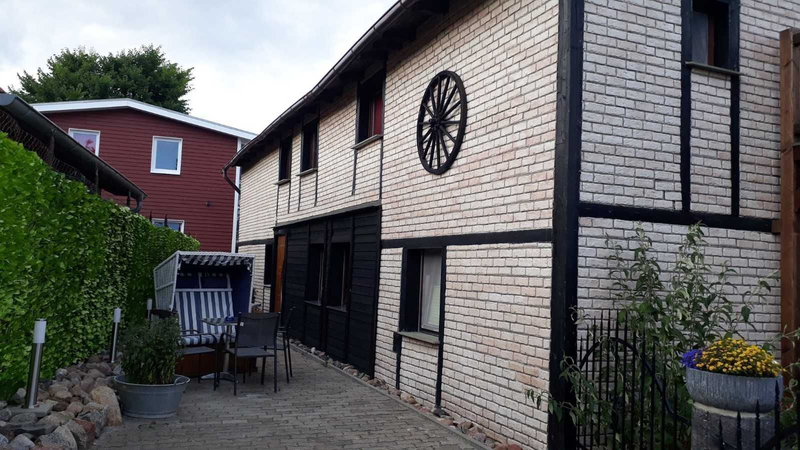 Ein Backsteinhaus mit einer großen Uhr an der Seite, einem kleinen Außenbereich mit Stühlen und einem Tisch sowie einem Blumentopf.