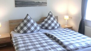 Ein Doppelbett mit karierter Bettwäsche, zwei Kissen, ein Nachttisch mit Lampe und ein Meeresbild an der Wand.