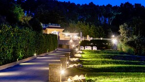 A well-lit pathway leading to a house with a stone wall and a fence.