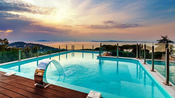 A swimming pool with a wooden deck, surrounded by metal railings, overlooking a scenic landscape with hills and a body of water.