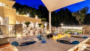 An outdoor dining area with a stone table, white chairs, and blue placemats.