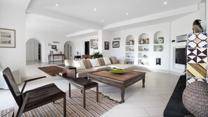 A spacious living room with a sofa, coffee table, and chairs. There is a TV and a fireplace.