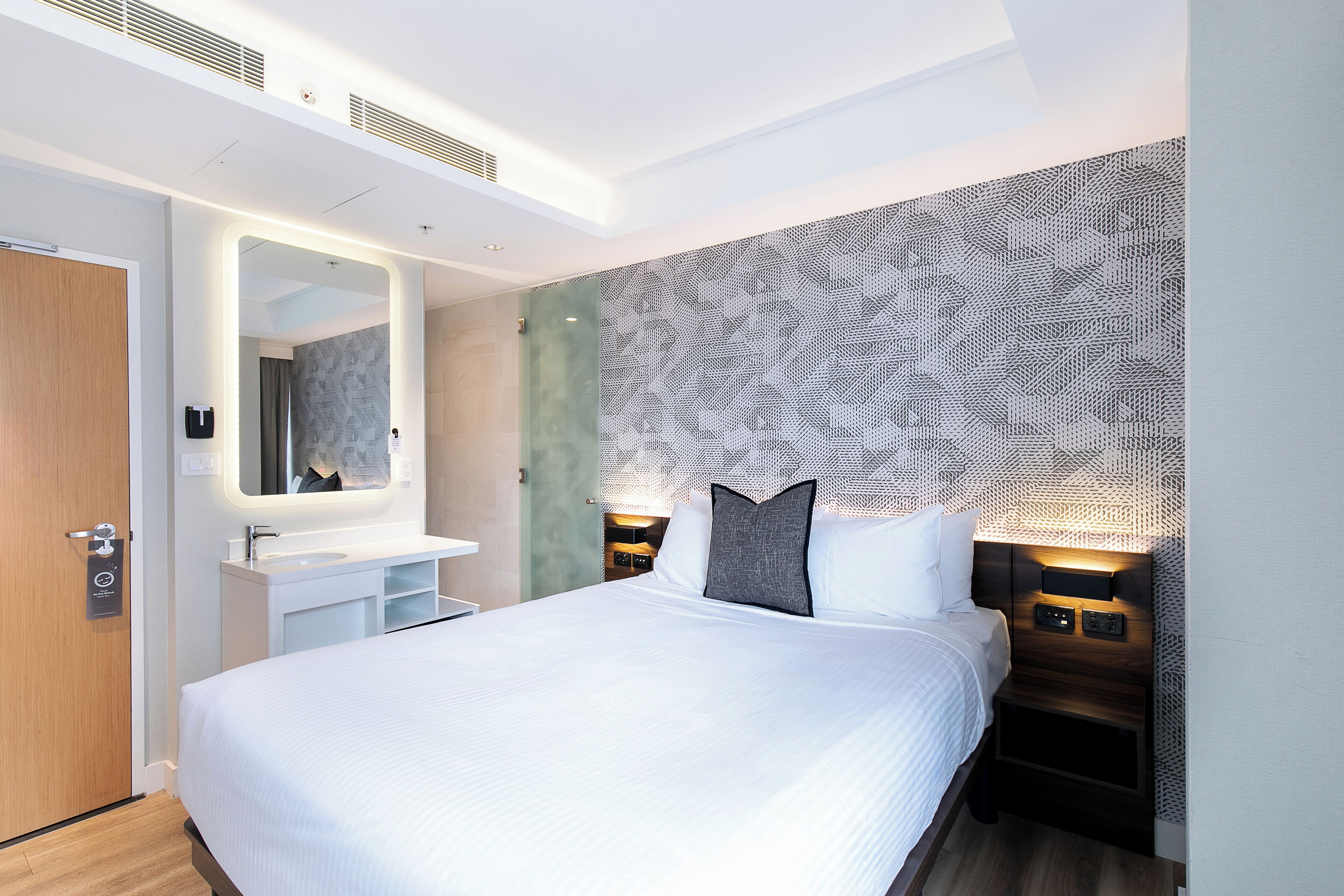Una camera d'albergo moderna con un letto grande, una toeletta integrata e una parete decorata.