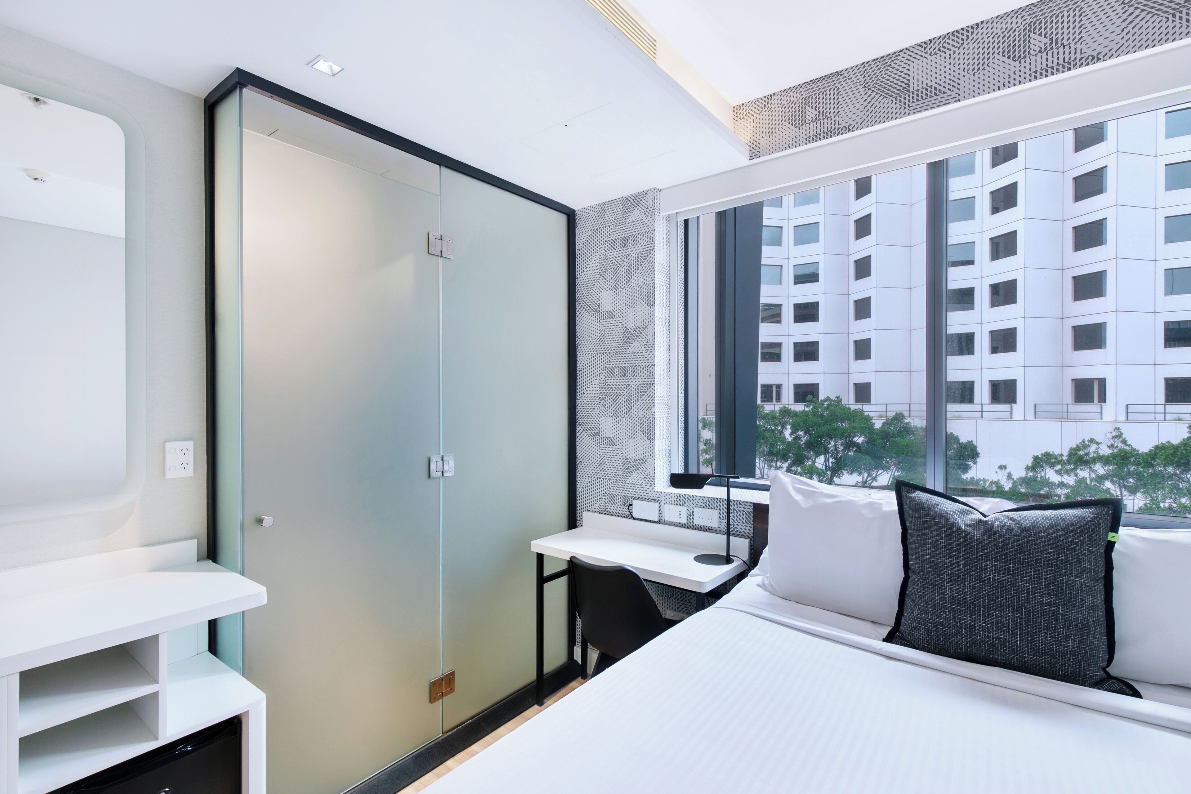 A modern hotel room with a bed, a desk, and a wardrobe.