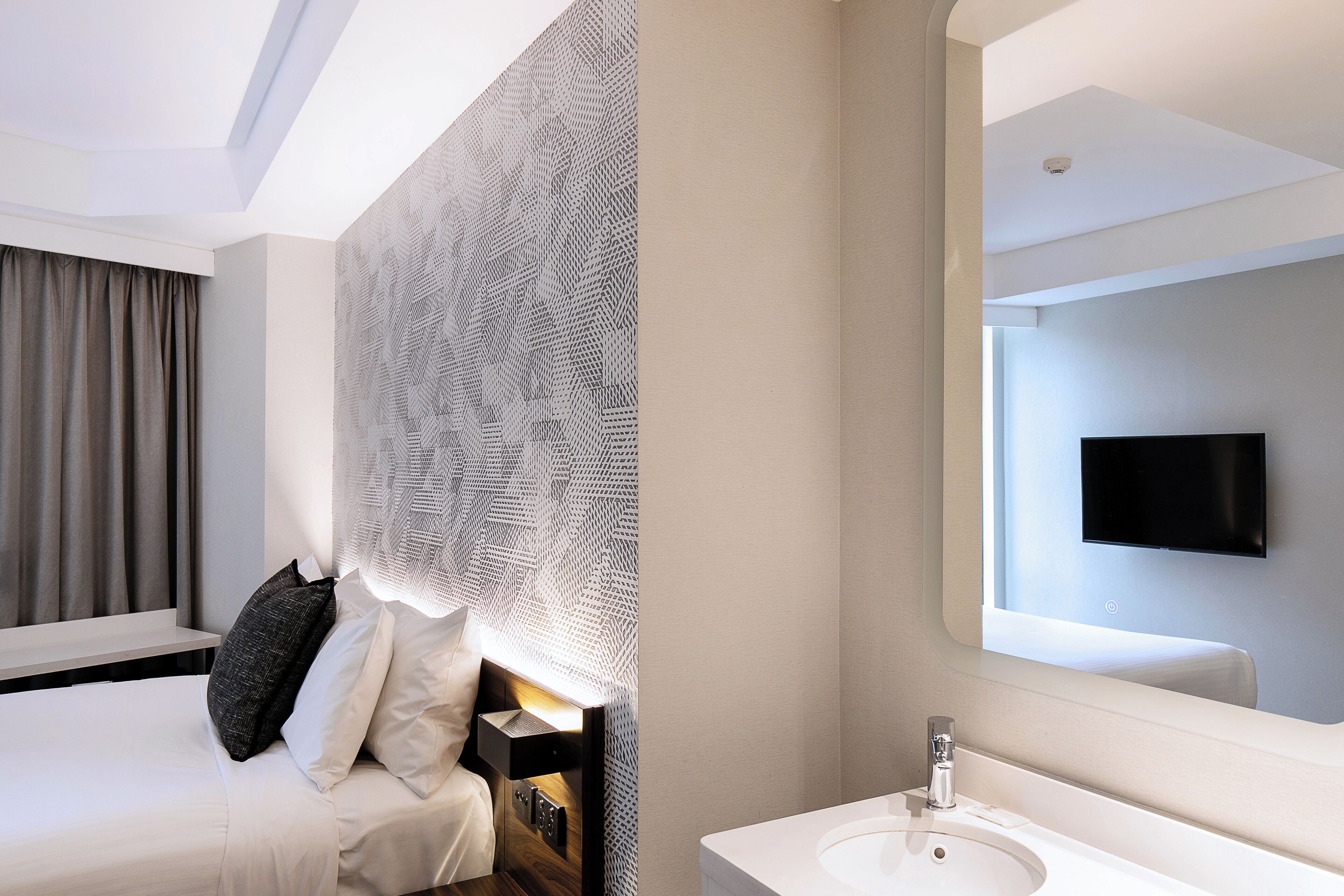 Een moderne hotelkamer met een bed, een grote spiegel, een televisie en een badkamer met een wastafel.