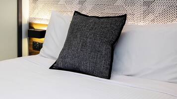 A neatly made bed with white linens and a single dark-textured pillow.