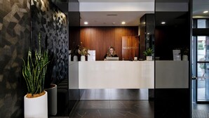 A reception area with a wooden panel wall, a reception desk, and a potted plant. - Kith Hotel Darling Harbour (Pyrmont)