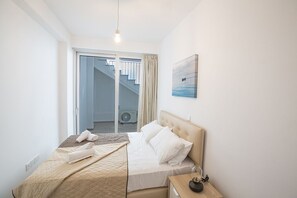 A hotel room with a bed, a nightstand, a painting, and a view of a staircase and outdoor area.