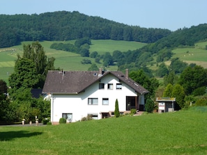 A two-story house with a sloped roof, surrounded by lush green fields and trees. - 5-star Fewo Baumkrone, directly at the Kellerwald-Edersee National Park - (Frankenau)
