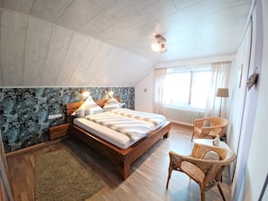 A bedroom with a wooden bed, a wicker chair, and a radiator. - 5-star Fewo Baumkrone, directly at the Kellerwald-Edersee National Park - (Frankenau)
