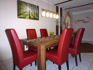 A dining room with a wooden table, six red chairs, a forest-themed wall art, a modern light fixture, and a decorative tree branch. - 5-star Fewo Baumkrone, directly at the Kellerwald-Edersee National Park - (Frankenau)
