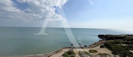 A coastal view with a beach, rocky shoreline, and a paved walkway.