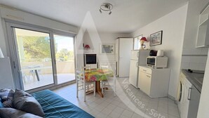 Un espacio habitable compacto con sofá, mesa de comedor, zona de cocina y puerta corrediza de vidrio que da a un área exterior.