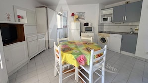 Una cocina compacta con muebles blancos, una mesa de comedor con mantel floral y una lavadora.