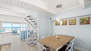 A modern interior with a wooden dining table, white chairs, a staircase, and artwork on the wall. - Ocean Colony 8 by Seaside Vacations & Sales (Ocean City)