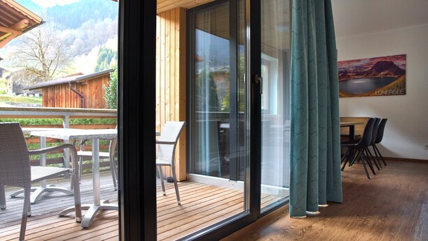 Une chambre moderne dotée d’une terrasse en bois, d’une porte-fenêtre coulissante donnant sur un espace extérieur et d’une table à manger avec des chaises.
